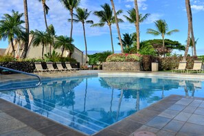 A swimming pool with lounge chairs, palm trees, and a view of the ocean.