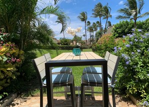 Een terras buiten met een tafel en stoelen, omgeven door weelderige begroeiing en palmbomen.