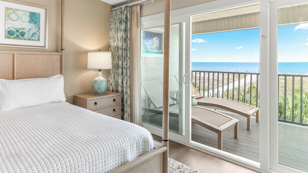 Une chambre à coucher avec un lit, une table de chevet, une lampe et une vue sur le balcon, où se trouvent une chaise et une table.