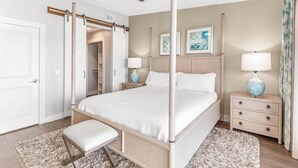 Une chambre à coucher avec un lit à baldaquin, un ventilateur de plafond, des lampes de chevet, une table de chevet, un banc et une porte donnant sur un placard.