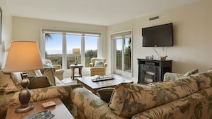 A living room with a sofa, armchairs, a coffee table, a TV, and a fireplace. - Shorewood 202 - Direct Oceanfront Beautiful Condo!! (Hilton Head Island)