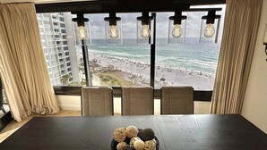 A room with a large window overlooking a beach and ocean, featuring a dark wooden table with a decorative bowl. - Large corner unit with spacious balconies! 4106 BS1 (Miramar Beach)