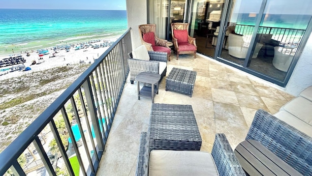 A balcony with wicker furniture, a view of the beach, and a pool. - Large corner unit with spacious balconies! 4106 BS1 (Miramar Beach)