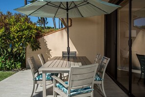 An outdoor patio with a table and chairs, an umbrella, and a glass door leading to a room.