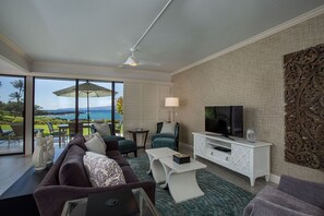 Ein modernes Wohnzimmer mit großem Fernseher, bequemen Sitzgelegenheiten, einem Balkon mit Meerblick und einem Deckenventilator.