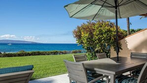 Een terras met een tafel en stoelen, een grote parasol en uitzicht op de oceaan.