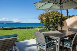 Un espace extérieur aménagé avec une table et des chaises, un grand parasol et une vue sur l’océan.
