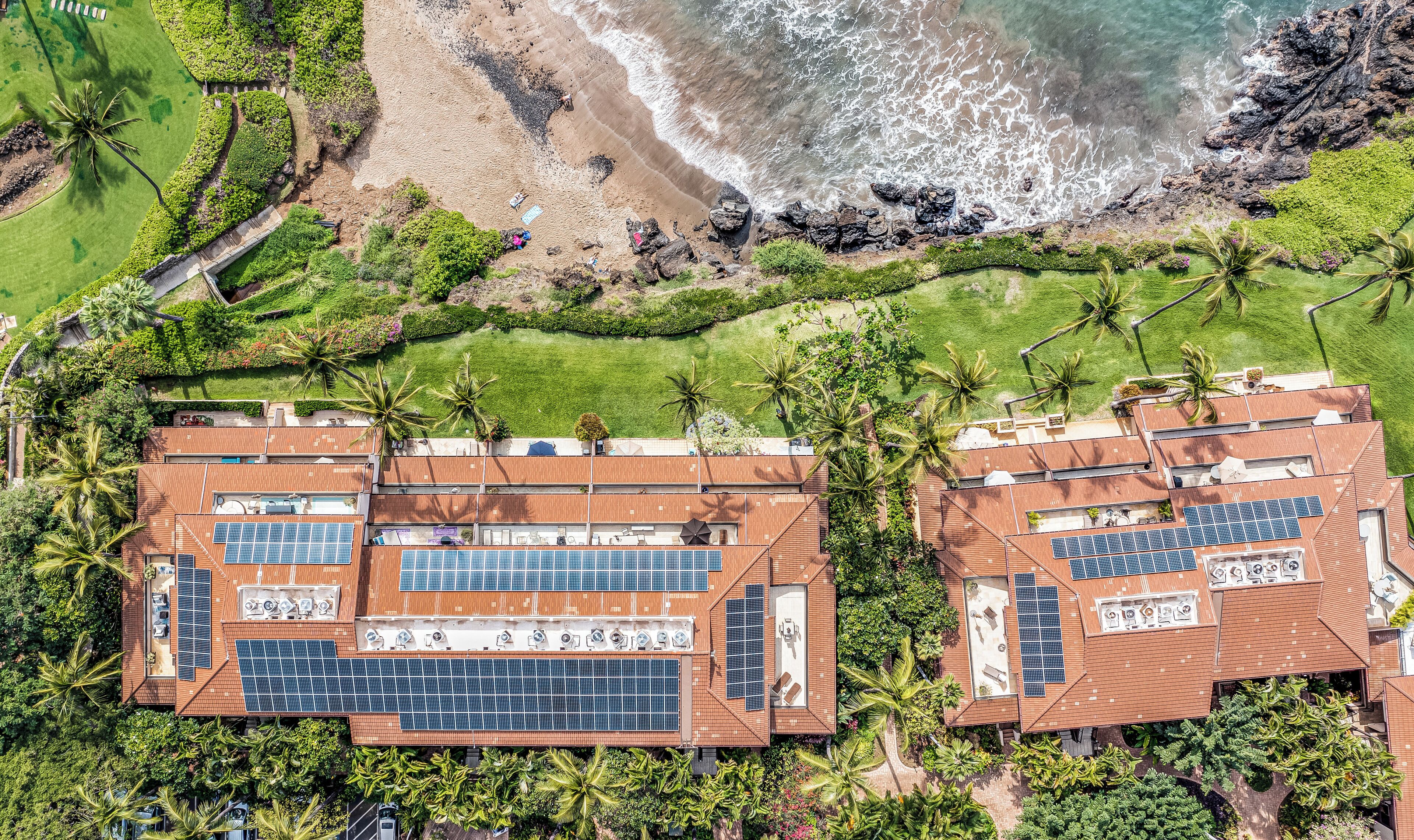 Un complexe hôtelier composé de plusieurs bâtiments dotés de panneaux solaires sur les toits, entouré d’une végétation luxuriante et bordé d’une plage.