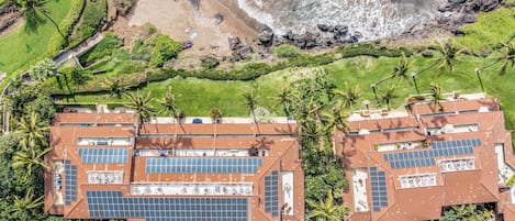 Un complexe hôtelier composé de plusieurs bâtiments dotés de panneaux solaires sur les toits, entouré d’une végétation luxuriante et bordé d’une plage.