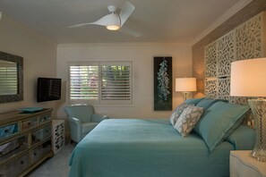 Un dormitorio con cama, una silla, ventilador de techo, televisor y ventana con persianas.