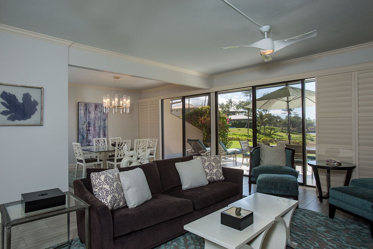A modern living room with a brown sofa, white coffee table, and a glass coffee table. There is a dining area with white chairs and a table in the background.