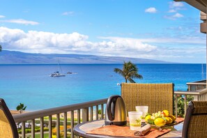 Enjoy a serene view of the sea and distant mountains from this balcony, complete with a refreshing drink and a selection of fresh fruit.