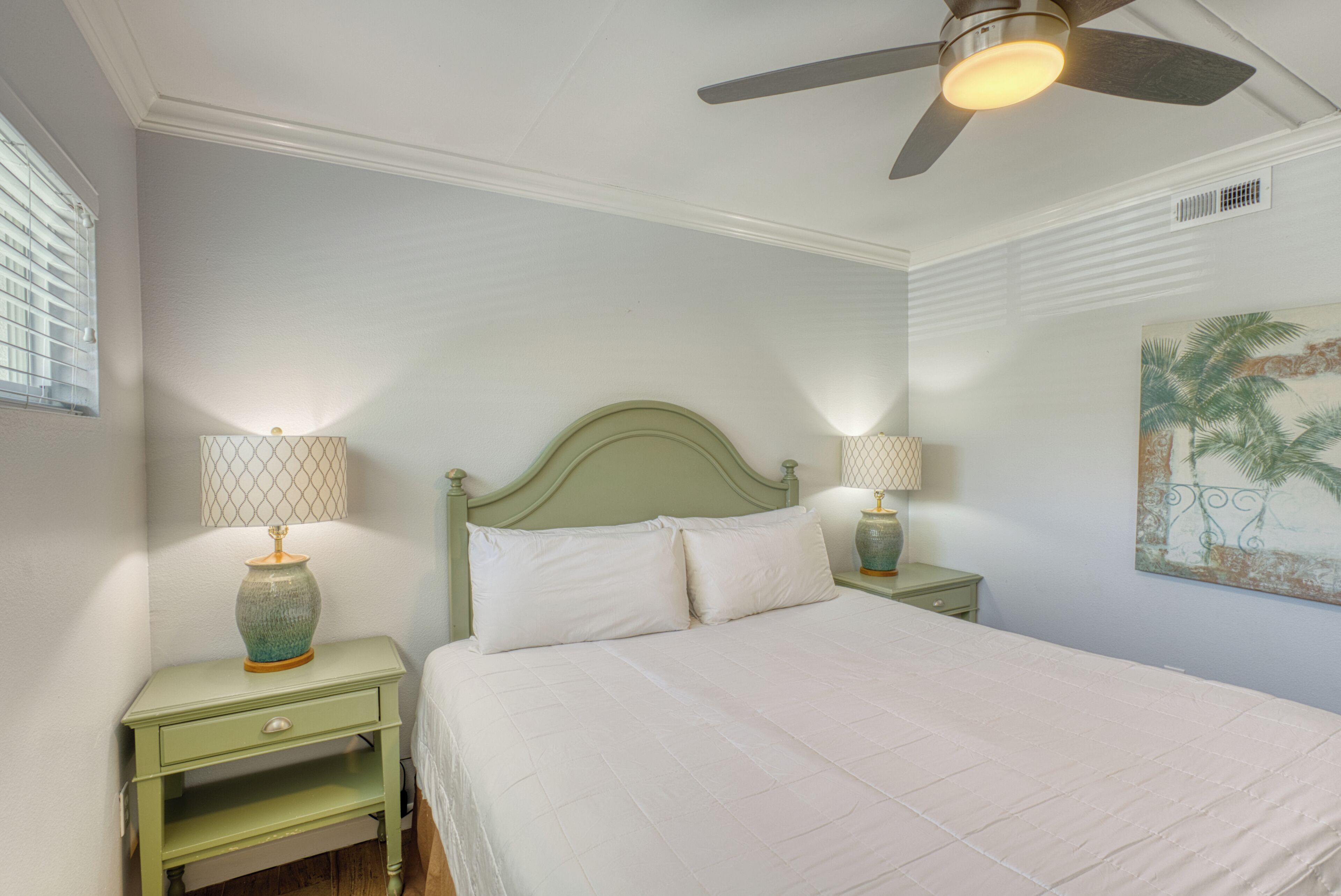 A bedroom with a bed, two nightstands, a ceiling fan, and a wall painting.