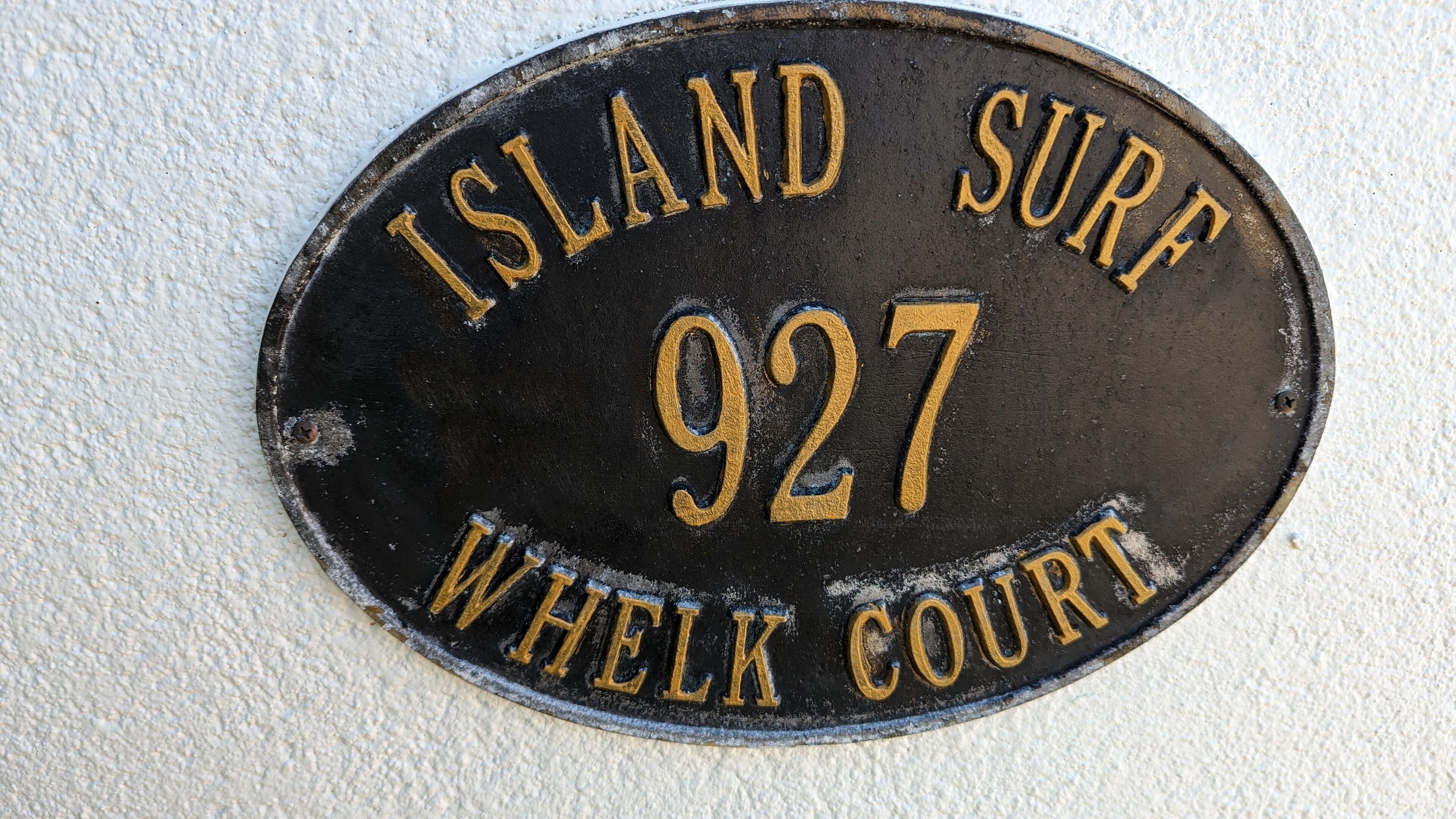 Musta metallikyltti, jossa on kultaisin kirjaimin kirjoitettu teksti: ”Island Surf, 927 Whelk Court”.
