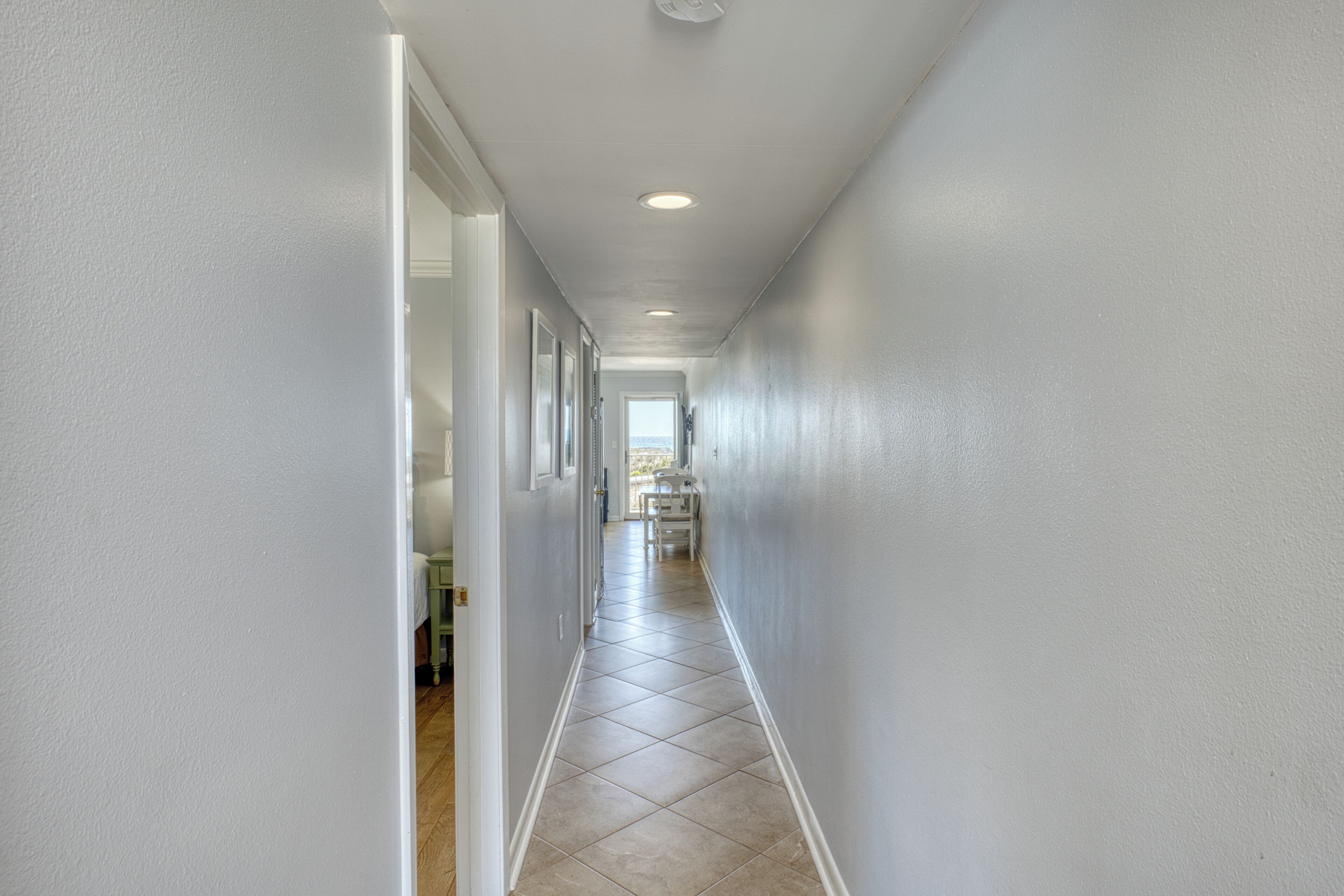 A hallway with white walls, a tiled floor, and recessed lighting.