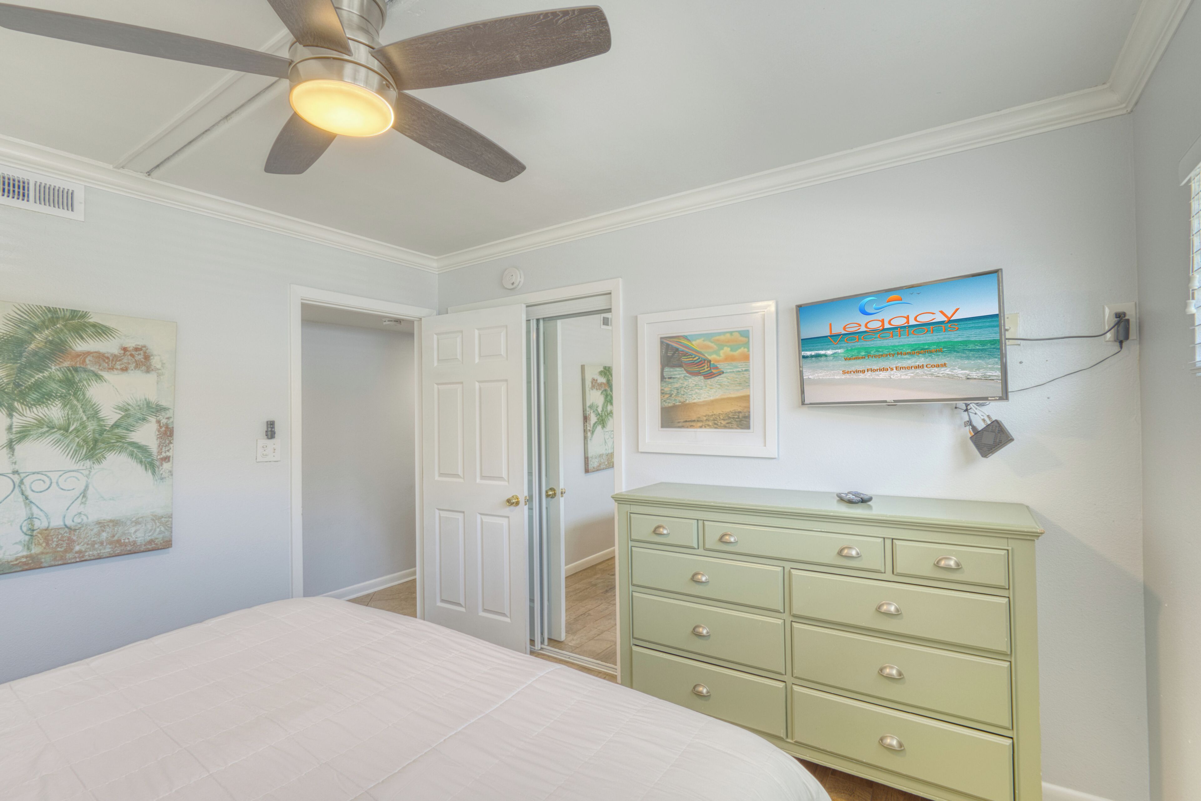 A bedroom with a bed, a ceiling fan, a dresser, and wall art.