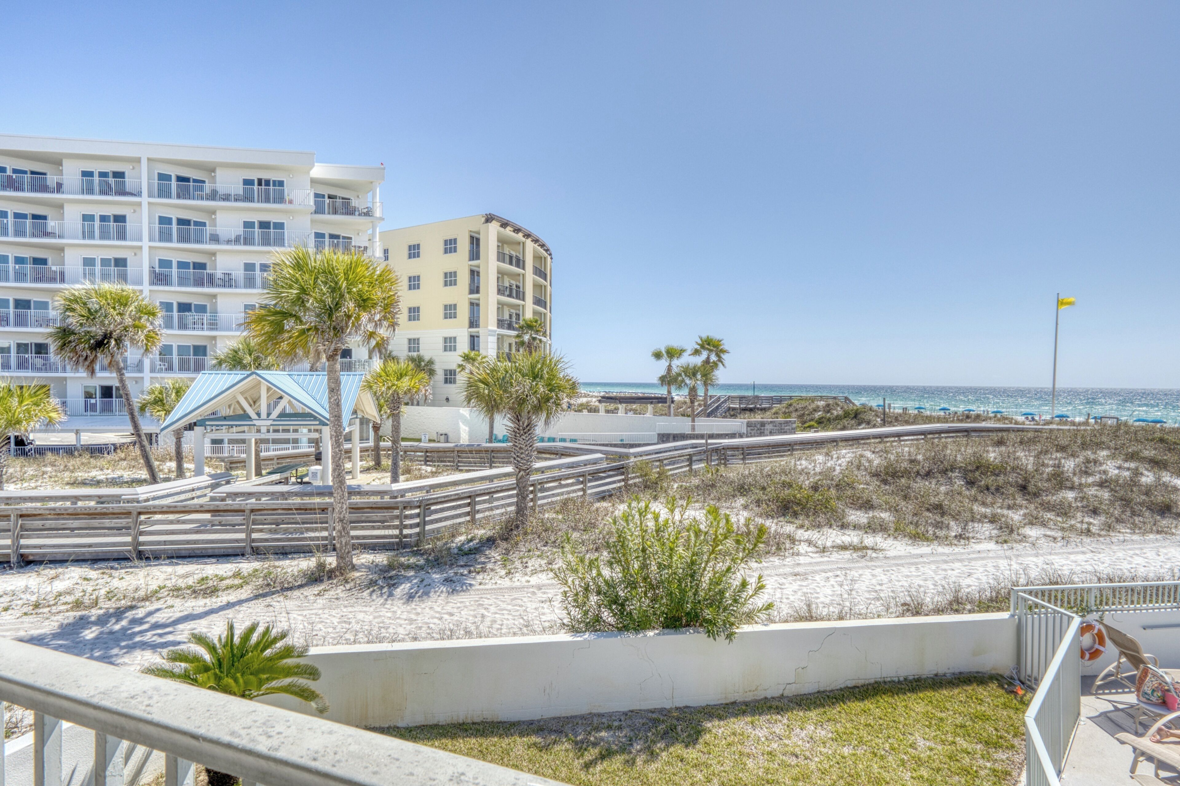 A beachfront hotel with multiple balconies, a beach area with palm trees, and a clear view of the ocean.