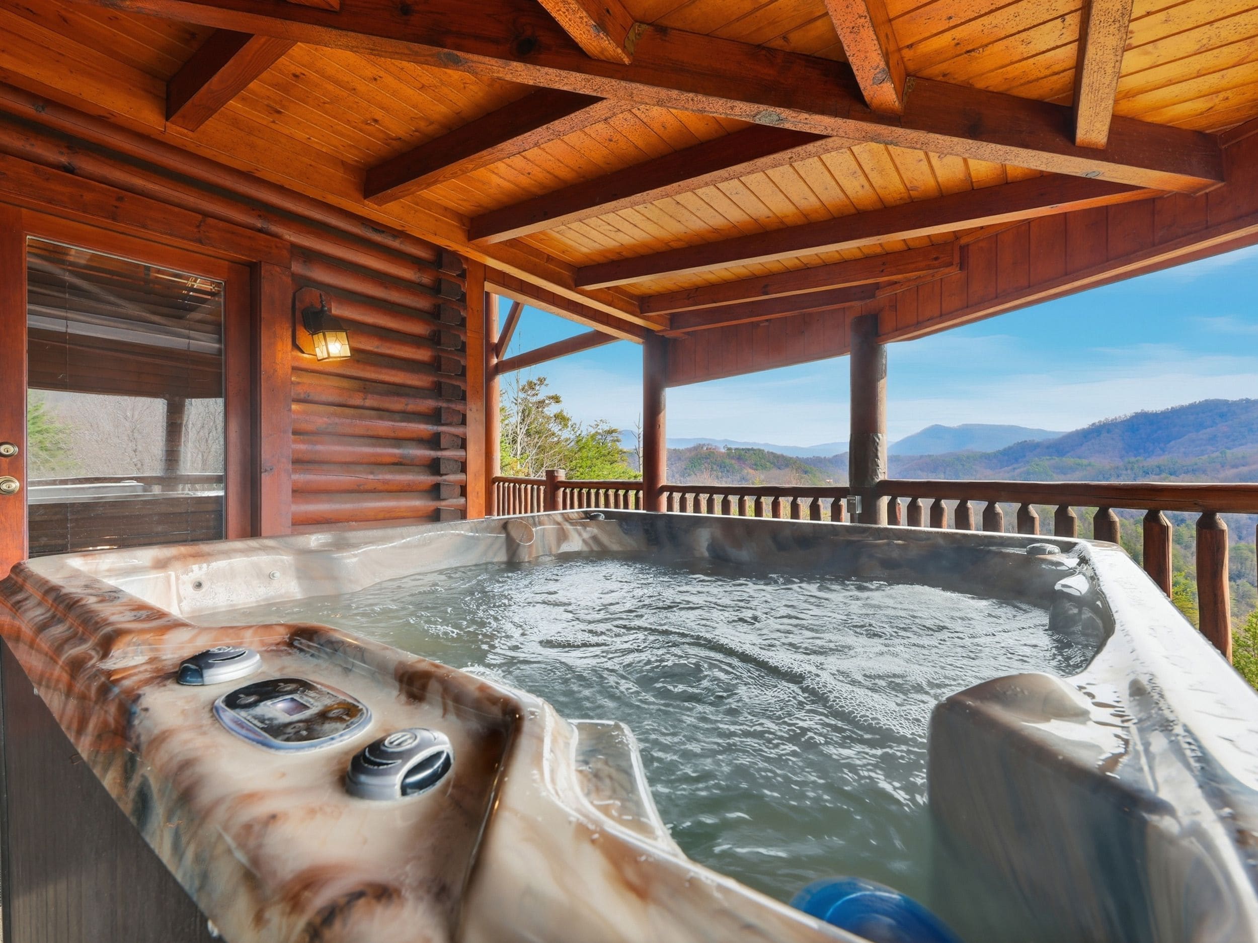 A wooden cabin with a hot tub and a view of the mountains.