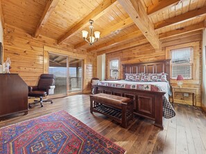 A log cabin bedroom with a large bed, a wooden bench, a chair, and a desk.