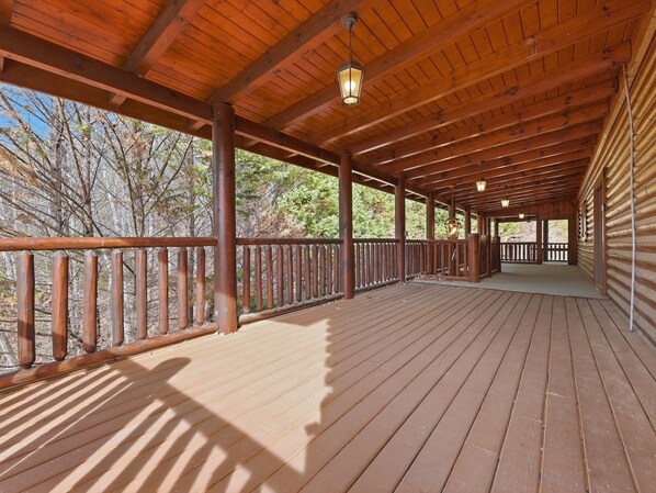 A wooden deck with a railing, supported by wooden beams and columns, overlooking a forested area.