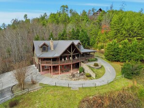 A large, two-story log cabin with a wrap-around porch and a stone fireplace. - Cabin w/Amazing Views, Large Game Room, Hot Tub (Sevierville)