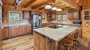 A spacious kitchen with wooden cabinets, granite countertops, a stainless steel refrigerator, and a central island with bar stools. - Cabin w/Amazing Views, Large Game Room, Hot Tub (Sevierville)