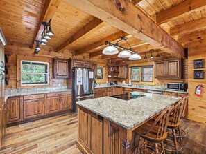 A spacious kitchen with wooden cabinets, granite countertops, a stainless steel refrigerator, and a central island with bar stools. - Cabin w/Amazing Views, Large Game Room, Hot Tub (Sevierville)