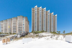 Un hotel frente a la playa con varios edificios altos, una playa de arena y un cielo azul despejado.