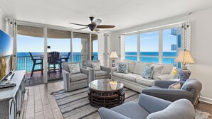 A spacious living room with a large window overlooking the ocean, furnished with a sofa, chairs, and a coffee table.