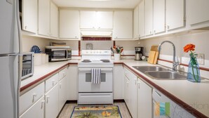 A kitchen with white cabinets, a microwave, stove, and a sink. - Direct Beach Access - Poolside Coastal Condo: Sea Gem (Palm Beach Shores)