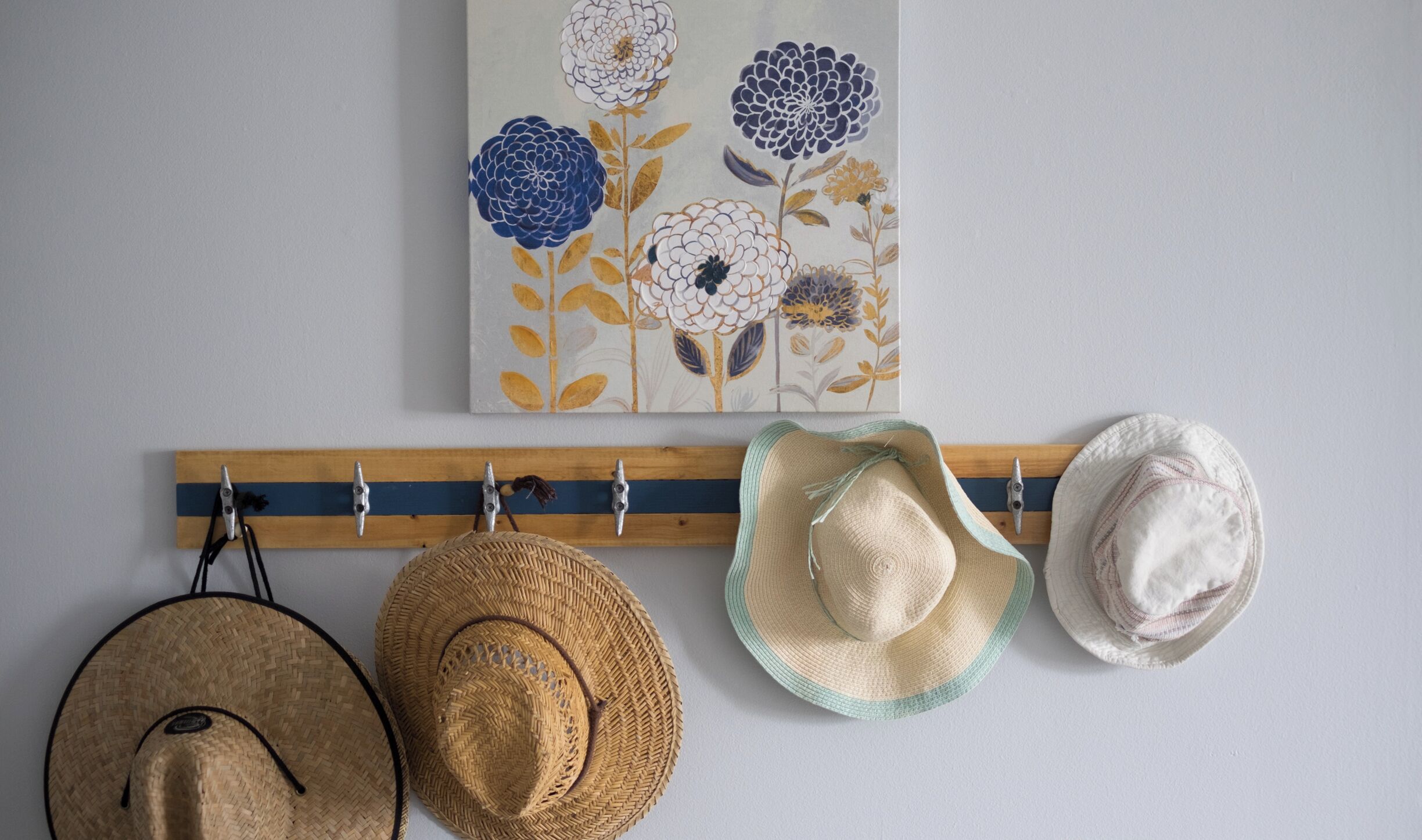 Un mur orné d’un tableau représentant des fleurs et un porte-chapeaux avec trois chapeaux.