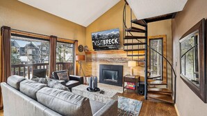 A living room with a fireplace, a sofa, a TV mounted above the fireplace, and a staircase leading to an upper level. - 4 O'Clock A16: Ski-In Condo, Gas Fireplace, 1 Block to Snowflake Lift. (Breckenridge)