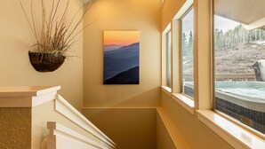 Ein Flur mit einem Gemälde einer Berglandschaft, einem Fenster mit Blick auf eine Whirlpool und einer Pflanze an der Wand.