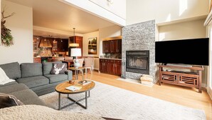 Ein modernes Wohnzimmer mit Sofa, Couchtisch, Kamin, Fernseher und einer Küche im Hintergrund.
