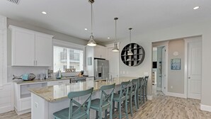 A modern kitchen with white cabinets, a central island with bar stools, and pendant lighting.