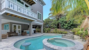 A two-story house with a backyard swimming pool and hot tub, surrounded by lush greenery and a wooden fence.