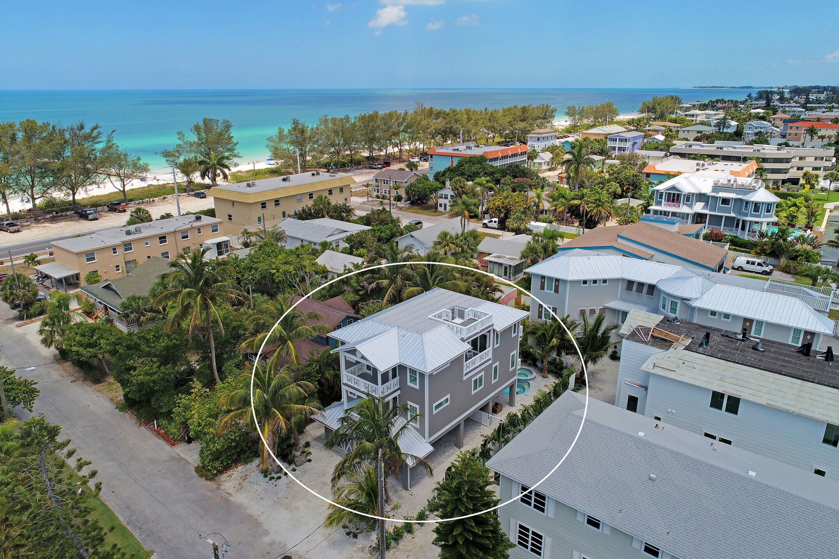 An aerial view of a coastal residential area with buildings, a beach, and a clear blue sky.
