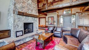 A spacious living room with a stone fireplace, leather sofas, and a red patterned rug.