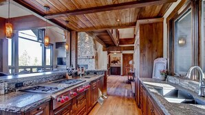 A spacious kitchen with wooden beams, granite countertops, and a large island with a stove and sink.