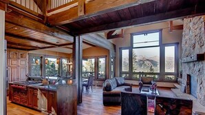 A spacious living area with a large window, wooden flooring, and a stone fireplace.