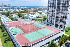 Un immeuble à plusieurs étages doté d’un court de tennis sur le toit, entouré d’immeubles résidentiels et offrant une vue sur l’océan.