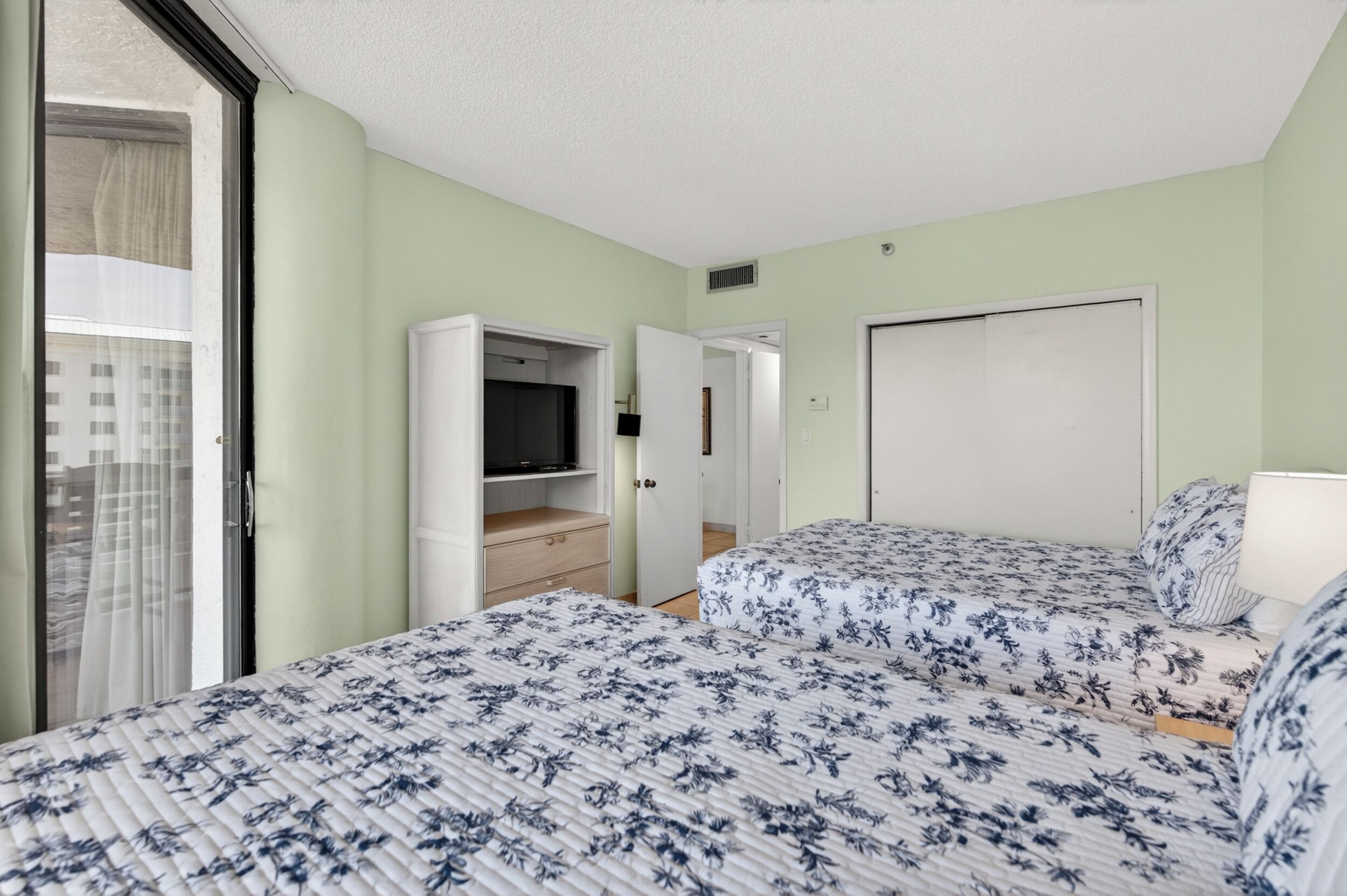 Ein Hotelzimmer mit zwei Betten, einem Fernseher, einem Kleiderschrank und einer Schiebetür zum Balkon.