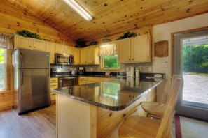 A wooden cabin-style kitchen with a granite countertop, stainless steel appliances, and a view of the outdoors through a window.