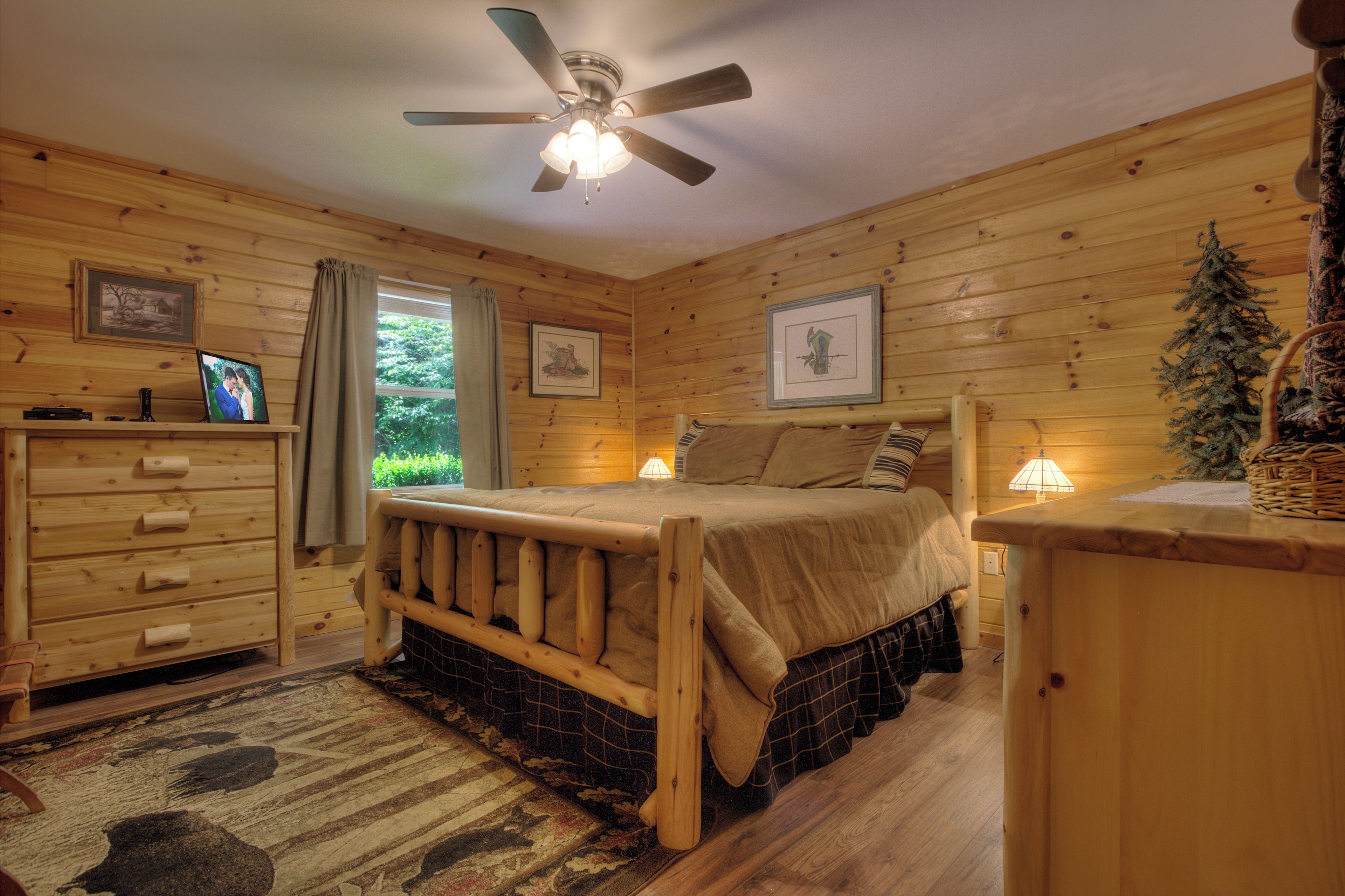 Une chambre dans un chalet en rondins, avec un lit, une commode et un ventilateur de plafond.