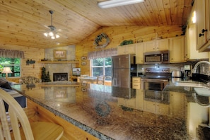 A spacious kitchen with granite countertops, stainless steel appliances, and wooden cabinetry. - Private Hot Tub | Soothing River Sounds | Scenic Outdoors (SEVIERVILLE)