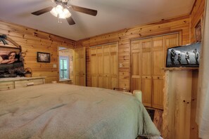 A bedroom with wooden paneling, a bed, a ceiling fan, and a television.