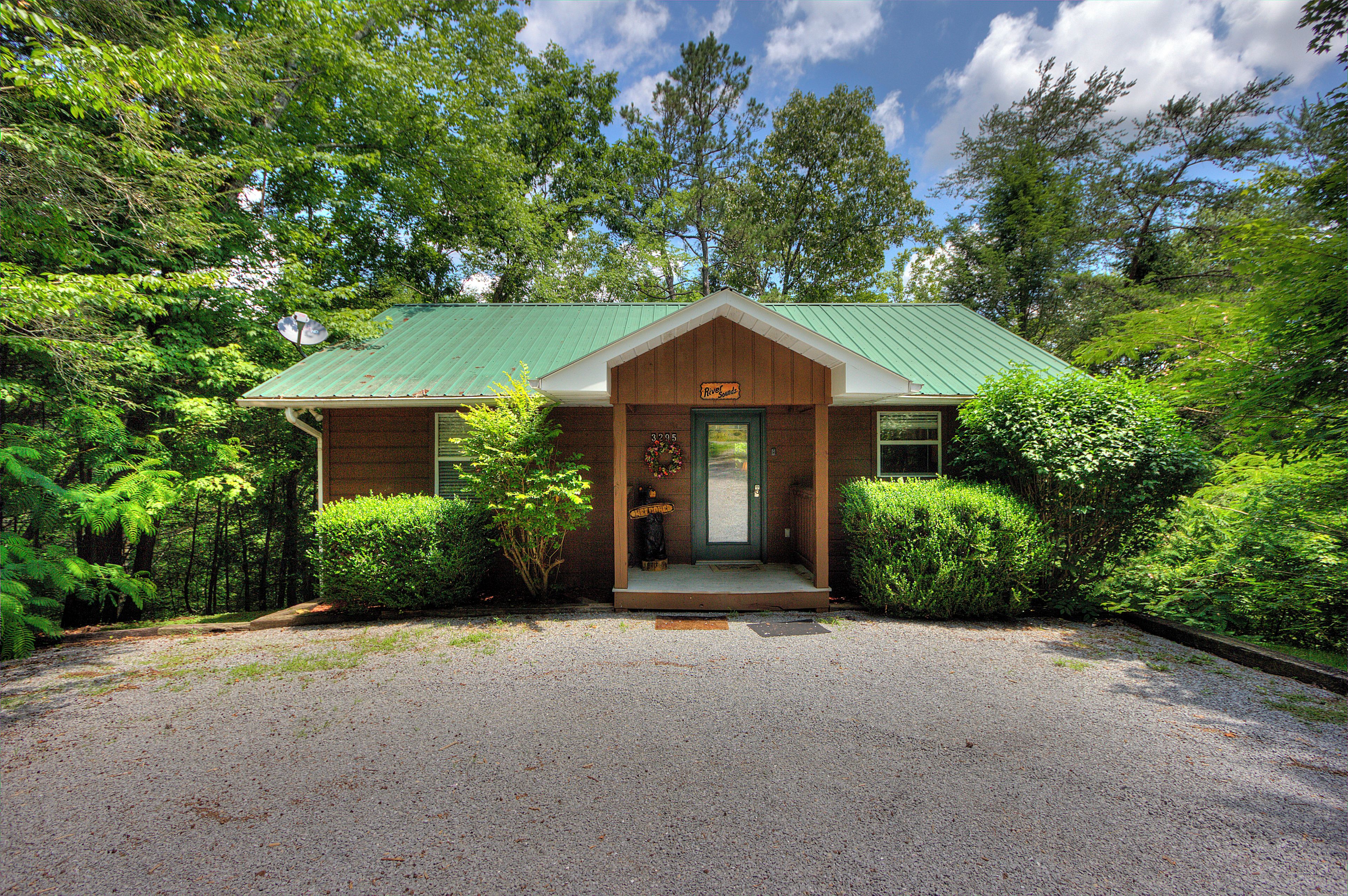 A lodge with a green metal roof, a wooden front porch, and a gravel driveway.