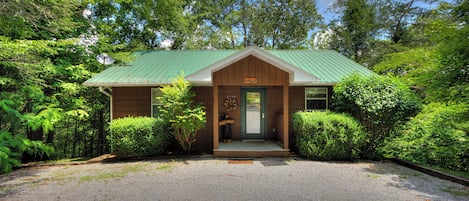 A lodge with a green metal roof, a wooden front porch, and a gravel driveway.