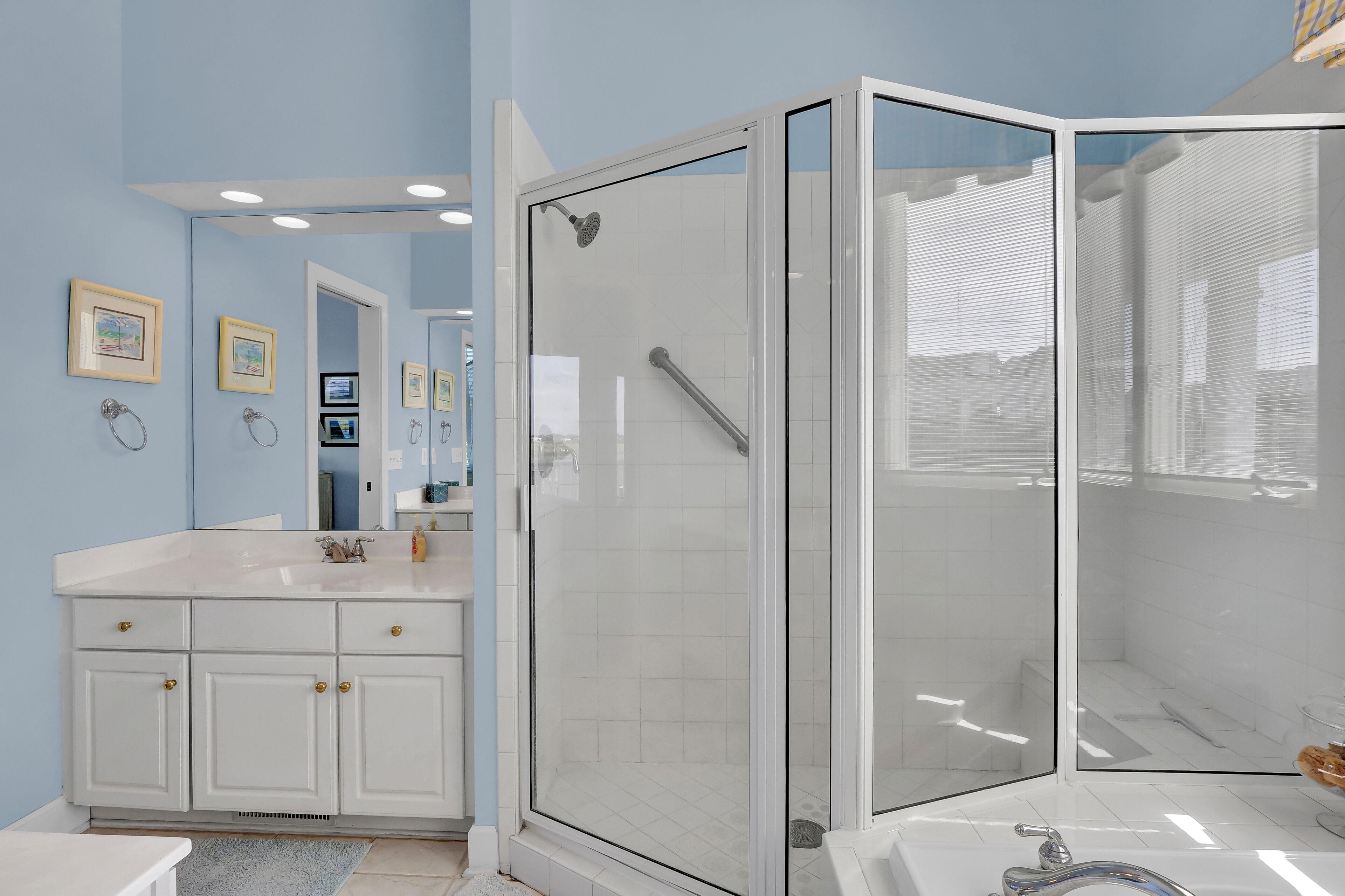 A bathroom with a glass-enclosed shower, a white vanity with a mirror, and framed pictures on the wall.