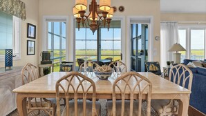 Un comedor con mesa y sillas de madera, una araña y vistas al exterior.